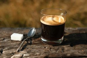 Une tasse remplir d'amour Close-up of espresso with sugar cube and spoon on rustic wooden surface outdoors in warm sunlight.